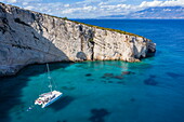 Luftaufnahme, Katamaran mit Menschen, die in einer abgelegenen Bucht mit Klippen schwimmen, Volimes, Zakynthos, Ionische Inseln, Griechenland, Europa