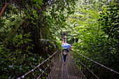 Young woman with umbrella crossing suspension bridge in the Lost Gardens of Heligan, near Mevagissey, Cornwall, England, United Kingdom, Europe