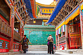 Tibetans walk around a richly decorated temple with prayer wheels and colored roof and ornaments at Kumbum Champa Ling Monastery, Xining, China