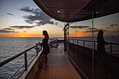 Frau steht an Reling und bewundert den Sonnenuntergang von an Bord Expeditionskreuzfahrtschiff World Voyager (nicko cruises), Pazifischer Ozean, in der Nähe von Panama, Mittelamerika