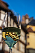 Half-timbered buildings and towers of the old town are reflected in a glass filled with white wine, Wertheim, Spessart-Mainland, Franconia, Baden-Wuerttemberg, Germany, Europe