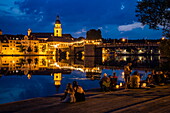 Menschen entspannen am Flussufer mit Spiegelung von Kirchen und Brücke im Main bei Nacht, Kitzingen, Franken, Bayern, Deutschland, Europa
