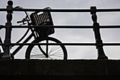Silhouette of a bicycle with a basket on a bridge over a canal, Amsterdam, North Holland, The Netherlands, Europe