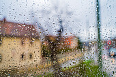 Water droplets on a window pane of an apartment building overlooking a farmhouse and a crossroads, Jena, Thuringia, Germany