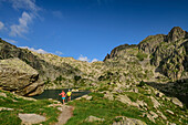 Man and woman hiking in Aigüestortes National Park, Estany del Barbs lake in background, Aigüestortes i Estany de Sant Maurici National Park, Pyrenees, Catalonia, Spain