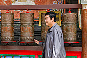 Ein lachender Mann dreht Gebetsmühlen an einem tibetischen Tempel im Kloster Kumbum Champa Ling bei Xining, China