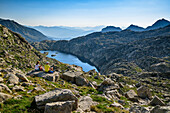 Man and woman hiking enjoying view of mountain lake, at Refugi Josep Maria Blanc, Aigüestortes i Estany de Sant Maurici National Park, Catalonia, Pyrenees, Spain
