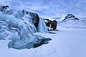 Der Berg Kirjufell in winterlicher Umgebung auf Island, im Vordergrund der gefrorene Wasserfall Kirkjufellsfoss, Island.
