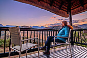 Woman sitting on terrace of Giant&#39;s Castle Lodge looking at Drakensberg, Giant&#39;s Castle, Drakensberg, Kwa Zulu Natal, Maloti-Drakensberg UNESCO World Heritage Site, South Africa