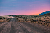 Cars creating a dust cloud on a gravel road through the Argentine pampas at dawn, Patagonia, South America