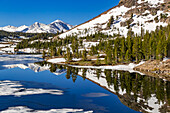 View of the crystal clear reflections of the mountains and trees on tranquil Lake Tioga in the pass of the same name, California, USA