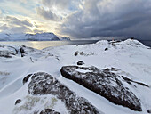 Snow-covered rock slabs on headland with bad weather clouds, Senja, Troms og Finnmark, Norway