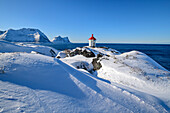 Leuchtturm steht auf Landzunge mit verschneiten Bergen im Hintergrund, Senja, Troms og Finnmark, Norwegen