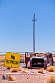 Rusted old car with bulletholes behind a sign that reads No Trespassing in the Arizona desert.