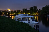 Ein Le Boat Tango Hausboot liegt am Ufer der Themse in der Abenddämmerung mit Schloss Windsor in der Ferne, Windsor, Berkshire, England, Vereinigtes Königreich