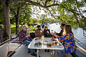 Friends enjoy wine and appetizers on deck of a Le Boat Horizon 4 houseboat moored on the River Thames, Henley-on-Thames, Oxfordshire, England, United Kingdom