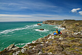 Mann und Frau beim Wandern sitzen an der Küste und blicken aufs Meer, GR 34, Zöllnerweg, Sentier Côtier, Halbinsel Crozon, Atlantikküste, Bretagne, Frankreich