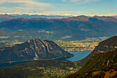 Luftaufnahme über eine wunderschöne Berglandschaft mit schneebedeckten Bergen und dem Luganersee und der Stadt Lugano an einem sonnigen Tag vom Monte Generoso, Tessin, Schweiz.