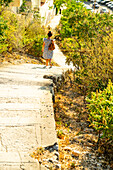 Woman walking down a sunny hillside staircase in Marseille, France.