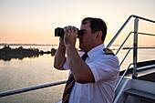 Captain Ion Ismana looks through binoculars from on board river cruise ship NickoVISION (Nicko Cruises) on the Danube, near Bratislava, Bratislava, Slovakia, Europe