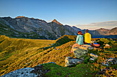 Mann und Frau beim Wandern sitzen auf Felsen und blicken auf Rosskopf und Höllenstein, vom Tettensjoch, Tuxer Tal, Zillertaler Alpen, Tirol, Österreich