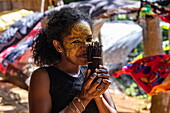Einheimische Frau mit Masonjoany-Gesichtsfarbe als Sonnenschutz riecht an Vanilleschoten auf dem lokalen Markt, Nosy Komba, Diana, Madagaskar, Indischer Ozean