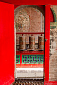 Gebetsmühlen hinter einem Tor in einem tibetischen Tempel der Klosteranlage Kumbum Jampaling im chinesischen Xining, Asien