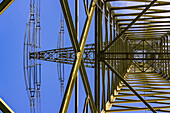Komplexe Stahlkonstruktion mit Traversen und Querverstrebungen von einem Hochspannungsmast mit Aufhängung für Stromleitungen von unten gesehen