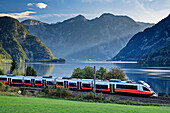  Train runs along Lake Hallstatt, Dachstein in the background, Salzkammergutbahn, Salzkammergut, Upper Austria, Austria 