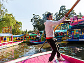 Popular tourist attraction people boating on colourful barges on canal at Xochimiloco, Mexico City, Mexico - trajinero punting barge