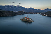  Bird&#39;s eye view of St. Mary&#39;s Church in Lake Bled and snowy mountains just after sunset in Bled, Slovenia, Europe. 
