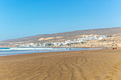 People walking along sandy beach at low tide near village of Taghazout, Morocco, North Africa