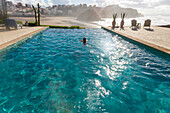 Frau schwimmt im Infinity-Pool am Atlantischen Ozean, Hotel Auberge Dar Najmat, Mirleft, Marokko, Nordafrika