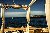 Blick vom balinesischen Bett auf der Terrasse des Hotels Sentido Fido Punta del Mar an der Costa de la Calma auf ein Segelboot in der Bucht bei Santa Ponca, Mallorca, Spanien
