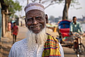 Porträt eines lächelnden Mannes mit weißem Bart und Fahrradrikscha dahinter, Chandpur, Distrikt Chandpur, Bangladesch, Asien