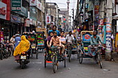 Menschen fahren mit Fahrradrikschas auf einer Straße in der Innenstadt, Barisal (Barishal), Bezirk Barisal, Bangladesch, Asien