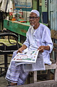 Älterer Mann mit Zeitung im Friseursalon, Kaukhali (Kawkhali), Bezirk Pirojpur, Bangladesch, Asien