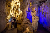  Couple admires illuminated stalactites and stalagmites in Trung Trang Cave on Cat Be Island, Lan Ha Bay, Haiphong, Vietnam, Asia 