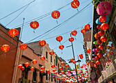 Red paper Chinese lanterns and umbrellas hanging above the street in Chinatown, Mexico City, Mexico advertising various restaurants