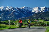 Mann und Frau fahren mit dem Rad am Bodensee-Königssee-Radweg, Mangfallgebirge im Hintergrund, Leitzachtal, Oberbayern, Bayern, Deutschland