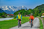 Mann und Frau fahren auf dem Bodensee-Königssee-Radweg an der Loisach entlang, Zugspitze im Hintergrund, Eschenlohe, Oberbayern, Bayern, Deutschland