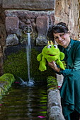  Woman in costume of the character “Princess” from the fairy tale “The Frog Prince” by the Brothers Grimm posing at the fountain, Steinau an der Straße, Spessart-Mainland, Hesse, Germany 