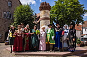  Locals in costumes of fairy tale characters from the Brothers Grimm pose in front of the fairy tale fountain in the old town, Steinau an der Straße, Spessart-Mainland, Hesse, Germany 