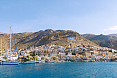  Island capital Póthia, white chapel, Greek flag, pastel-colored houses and boats in the harbor on the island of Kalymnos (Kalimnos) in Greece 