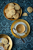 Sablés auf Teller mit Goldrand und Kaffee, mit blauem Untergrund 