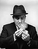 Mid-adult man in suit and hat lighting a cigarette