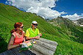  Man and woman hiking sitting on a bench and taking a break, Pfunderer Höhenweg, Zillertal Alps, South Tyrol, Italy 