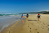 Drei Personen wandern über den Sandstrand von Nature's Valley, Otter Trail, Tsitsikamma Section, Garden Route National Park, Eastern Cape, Südafrika