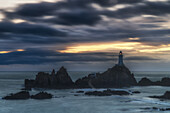  Lighthouse of Le Corbiere stands on rocky island surrounded by water during twilight. 