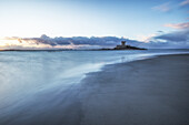  La Rocco Tower stands on the sandy beach at sunset. The sky is reflected in the water. 